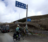 Bicyclist heading to Lhasa at 15,280 foot pass, with prayer flags on pass